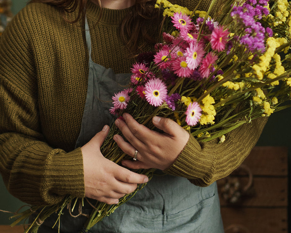 Person holding a bunch of pink and yellow statice flowers and pink daisy dried flowers