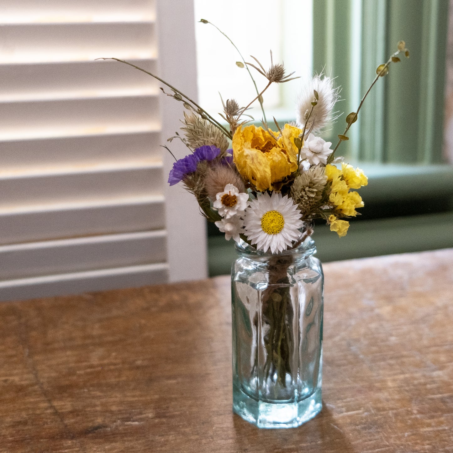 blue yellow and white dried flower mini posy displayed in a clear glass bud vase on a wooden table