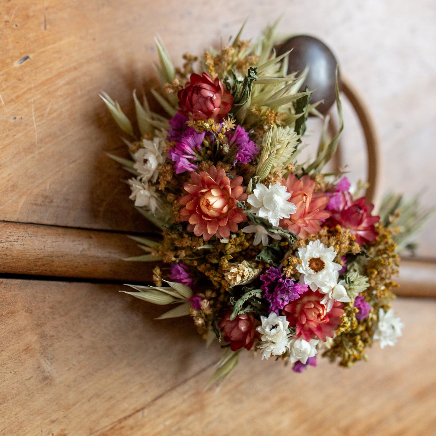 close up of a mini dried flower wreath with green, white and pink flowers, the wreath is hung on a wooden drawer knob