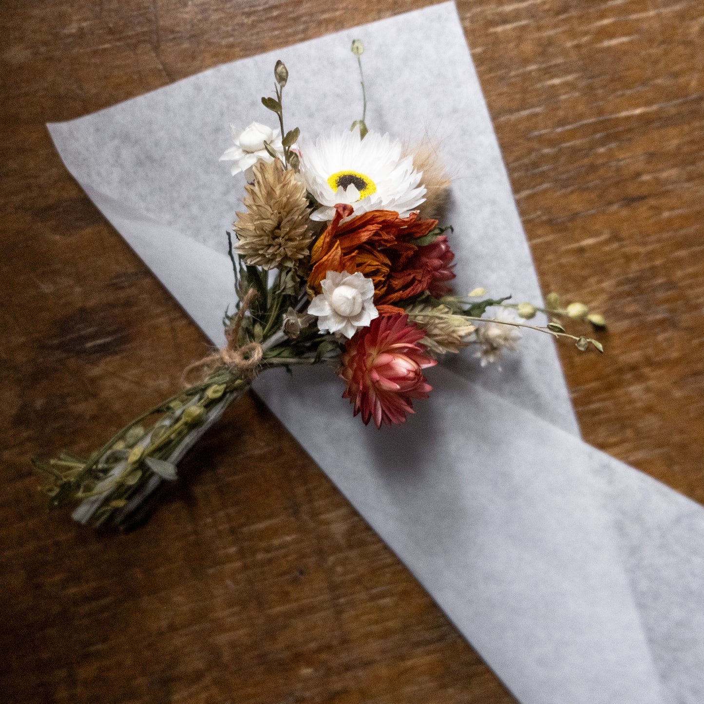 Dried flower posy arrangement laid on white tissue on a wood table