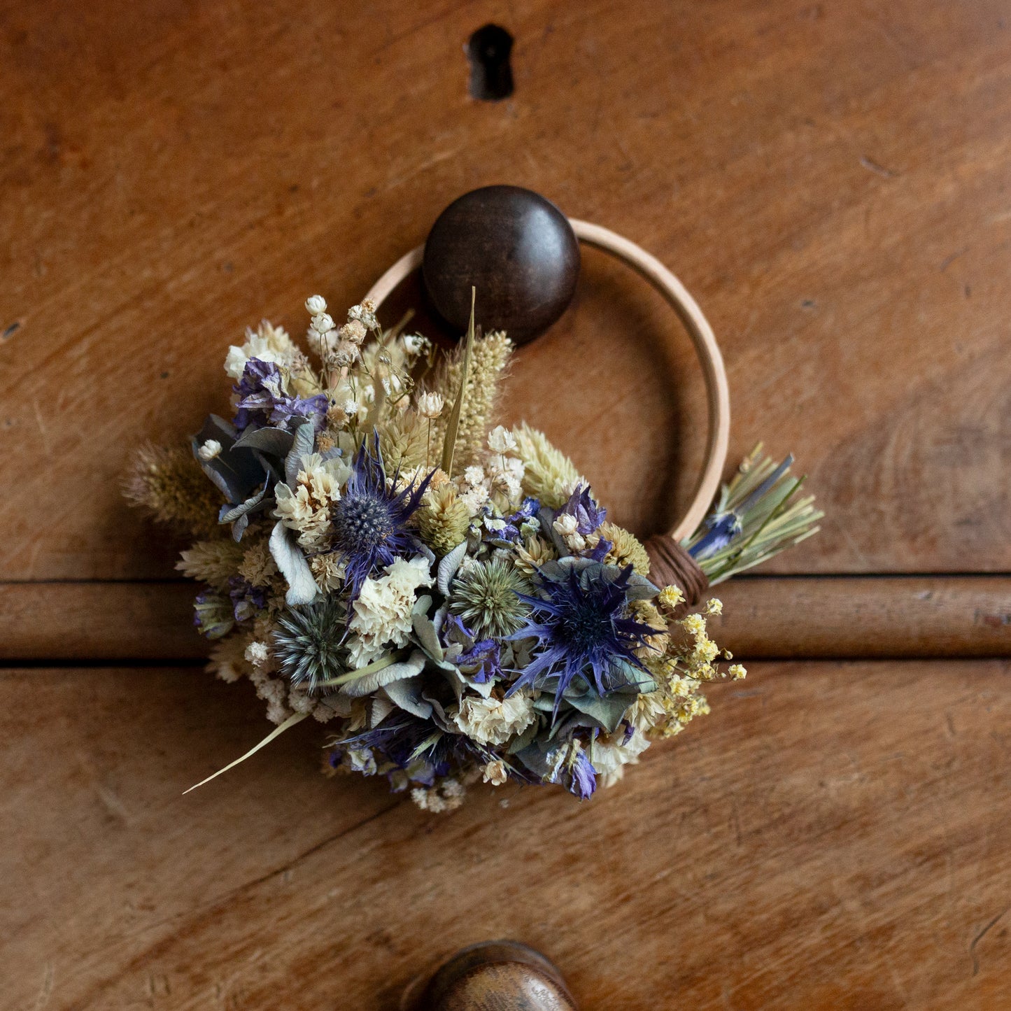 blue and white dried flower mini wreath hoop hung on wooden drawer knob. Flowers cover half of a wooden hoop