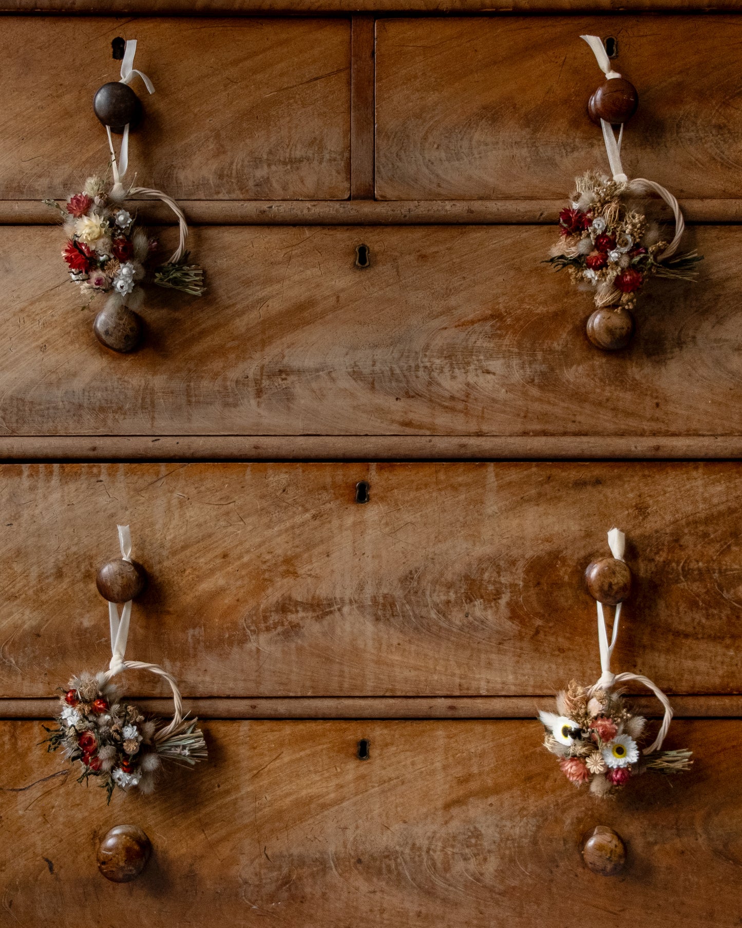 a dark wood chest of drawers with 4 small christmas wreaths hung with ribbon on 4 drawer handles