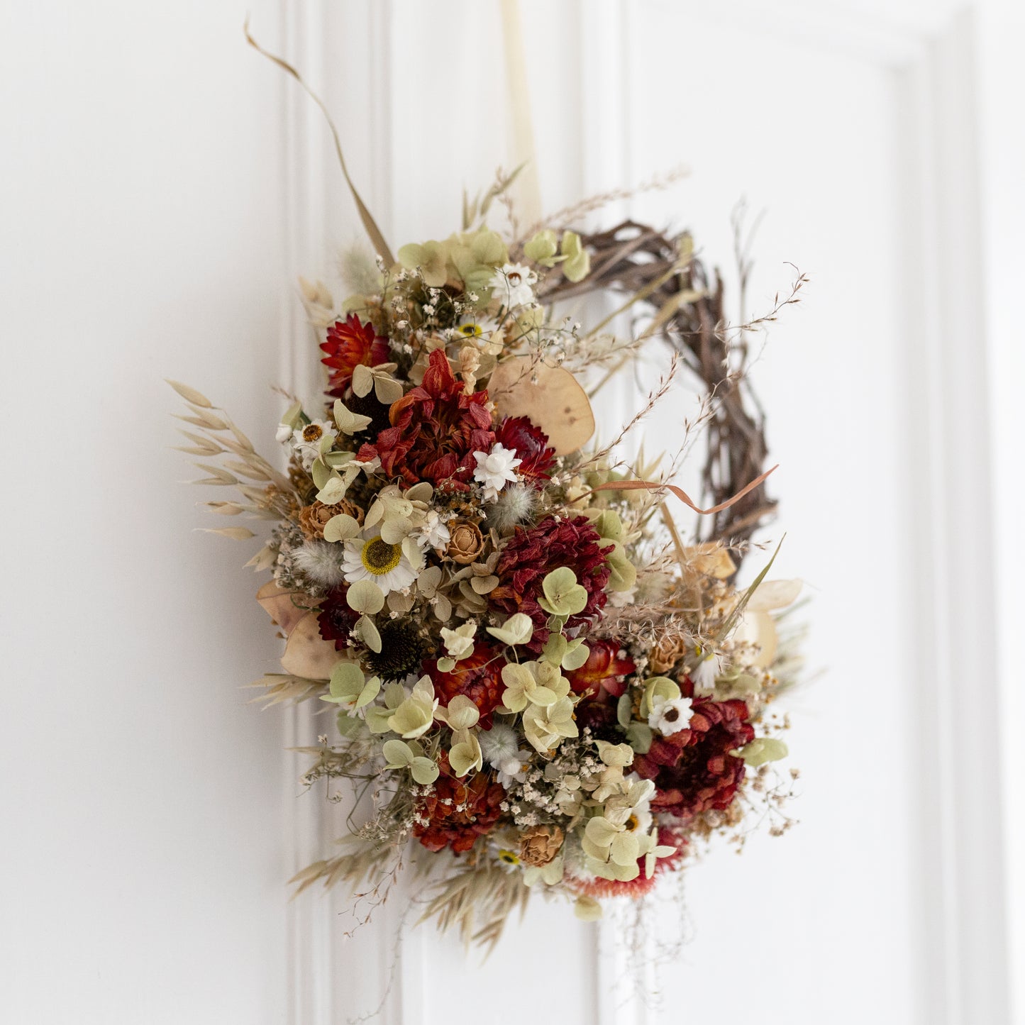 close up of dried flower wreath with autumnal flowers and leaves on a white door.