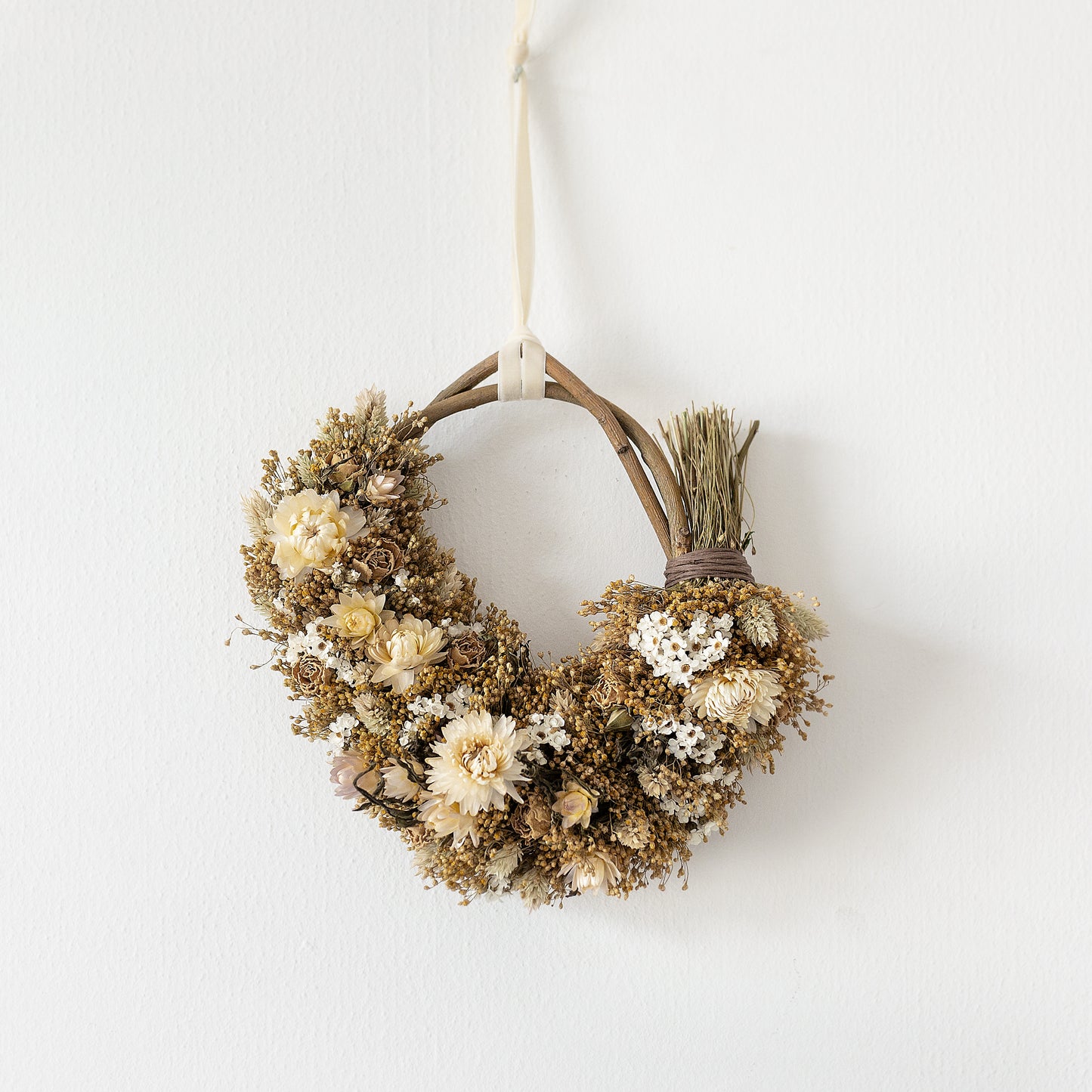 neutral white and golden dried flower wreath hung on a white wall