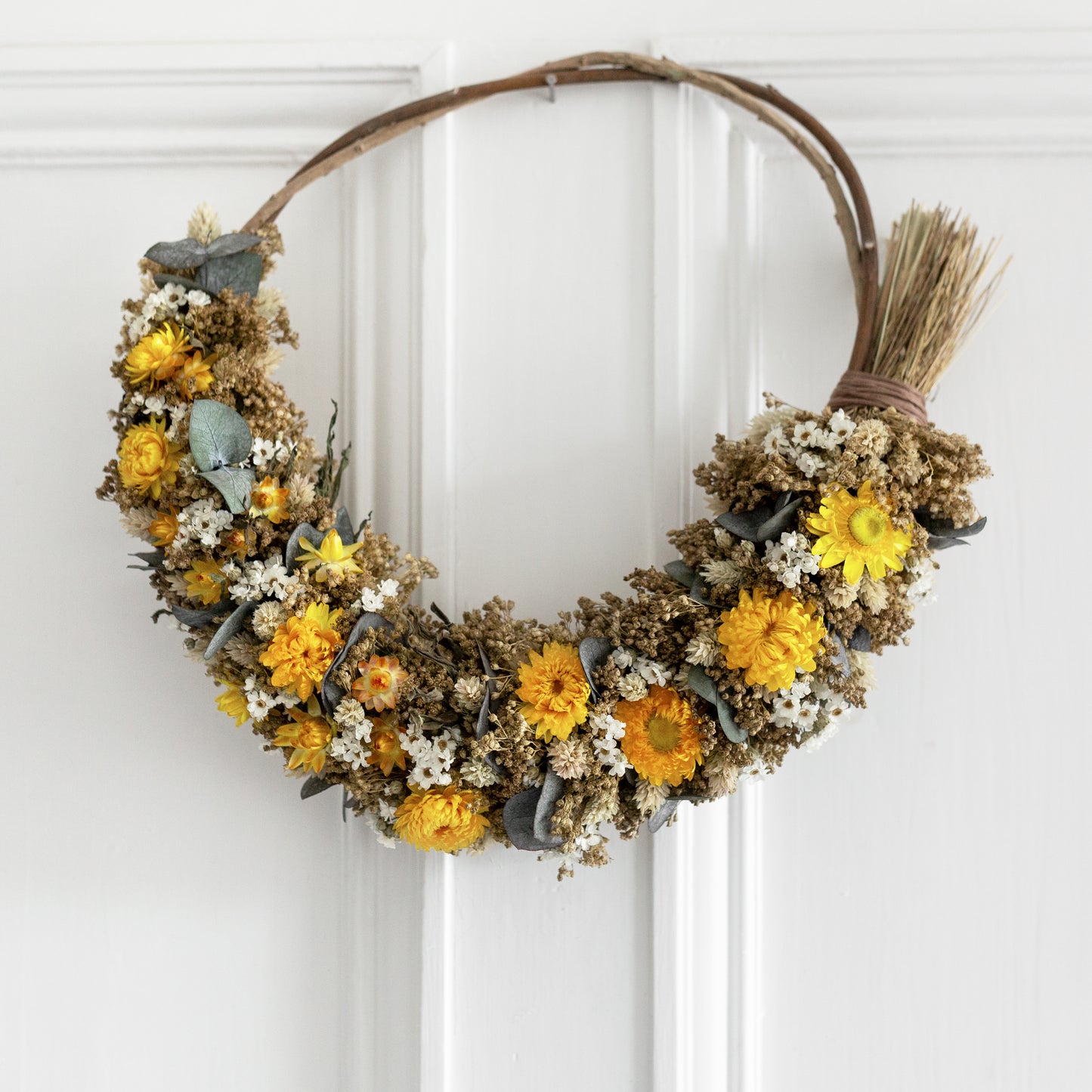 Decorative wreath with dried yellow and white flowers with eucalyptus hung on a white door