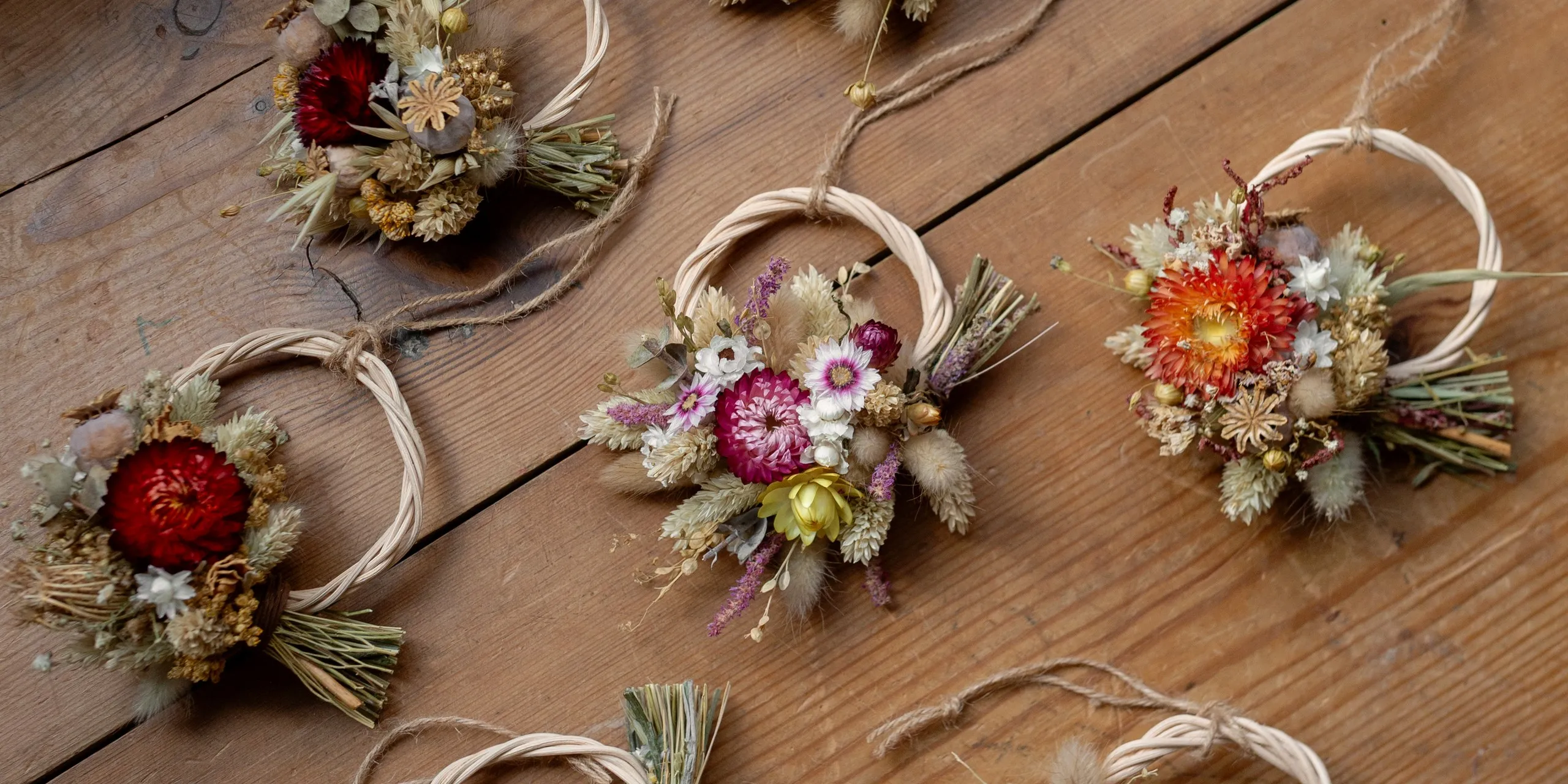 Small dried flower wreaths laid out on a wooden table.