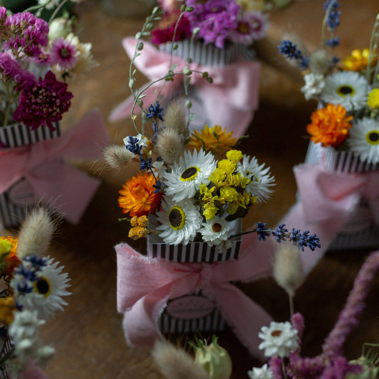 small bouquets in stripy gift boxes with a pale pink bow. bouquet in focus is made from orange, white, yellow and white dried flowers