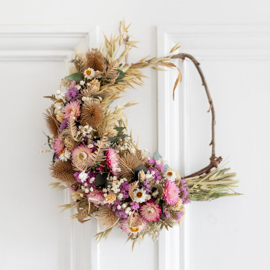 Decorative wreath made from dried flowers. Wreath is half covered in pink flowers, teasels, eucalyptus and grasses 