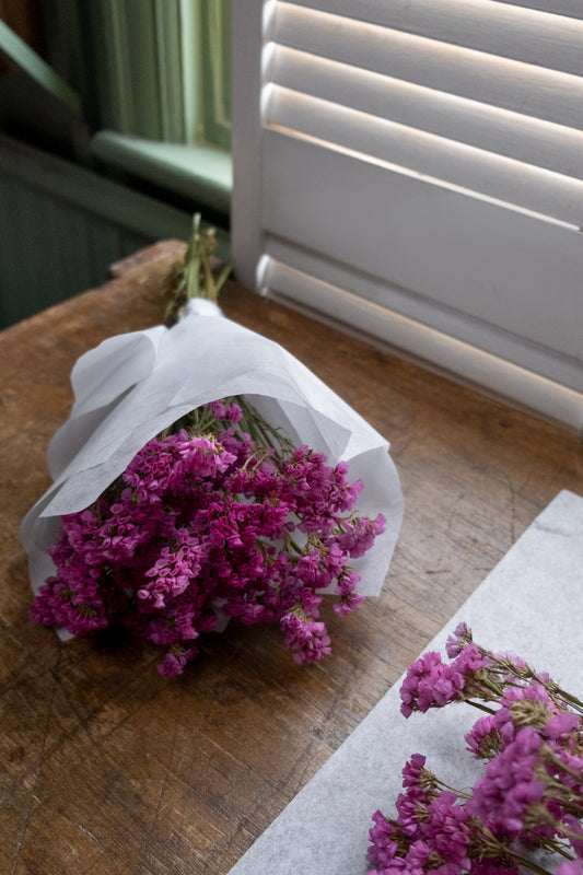 bunch of pink dried statice wrapped in white paper tied with twine laying on a wooden table top