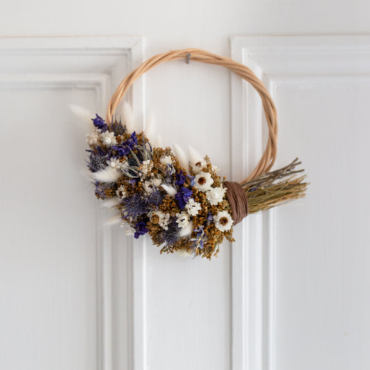 blue and white and golden coloured dried flowers covering half a wicker wreath hung on a white door
