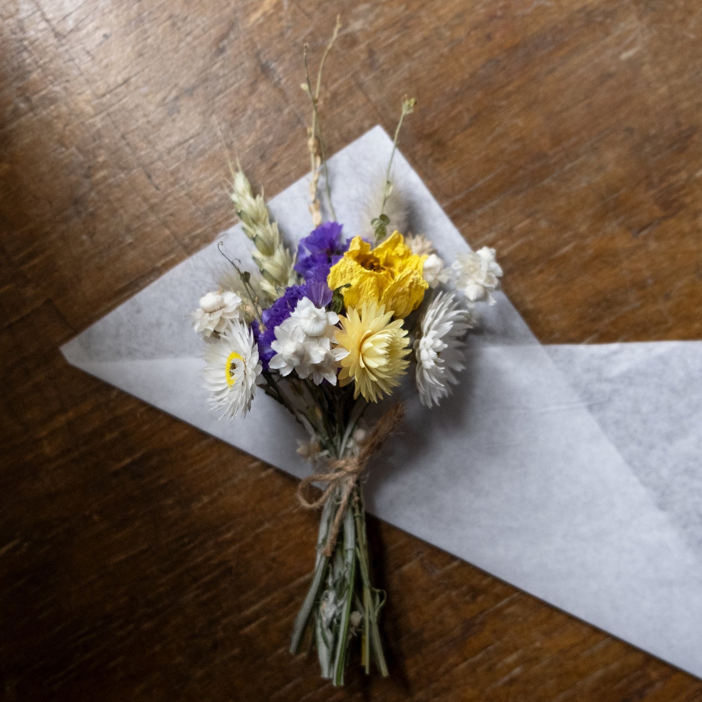 dried flower posy made up of blue, white and yellow flowers tied together with twine laid on a piece of white tissue paper on a wooden table