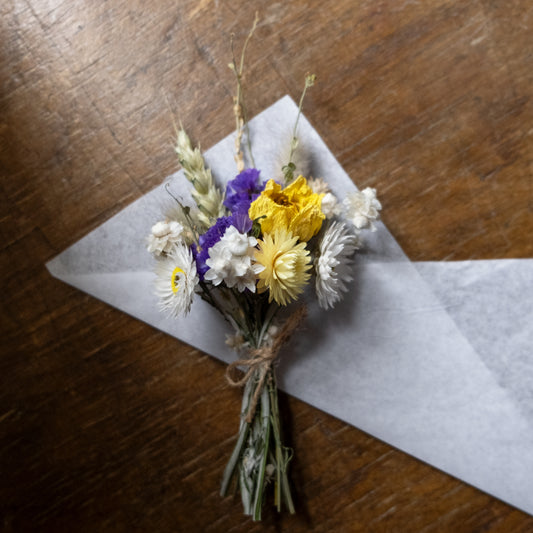 dried flower posy made up of blue, white and yellow flowers tied together with twine laid on a piece of white tissue paper on a wooden table