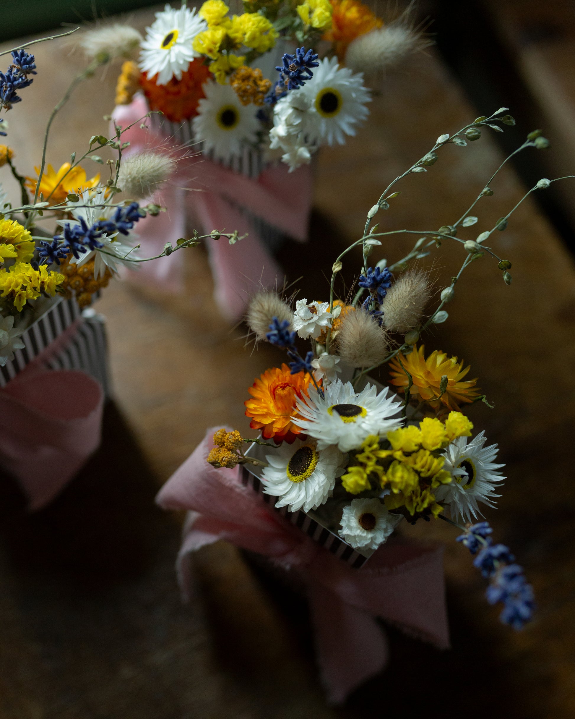 small bouquet of dried flowers with a blurred background, bouquet in focus is made of dried flowers yellow statice, orange strawflowers, lavender, bunny tails and grasses and white daisies