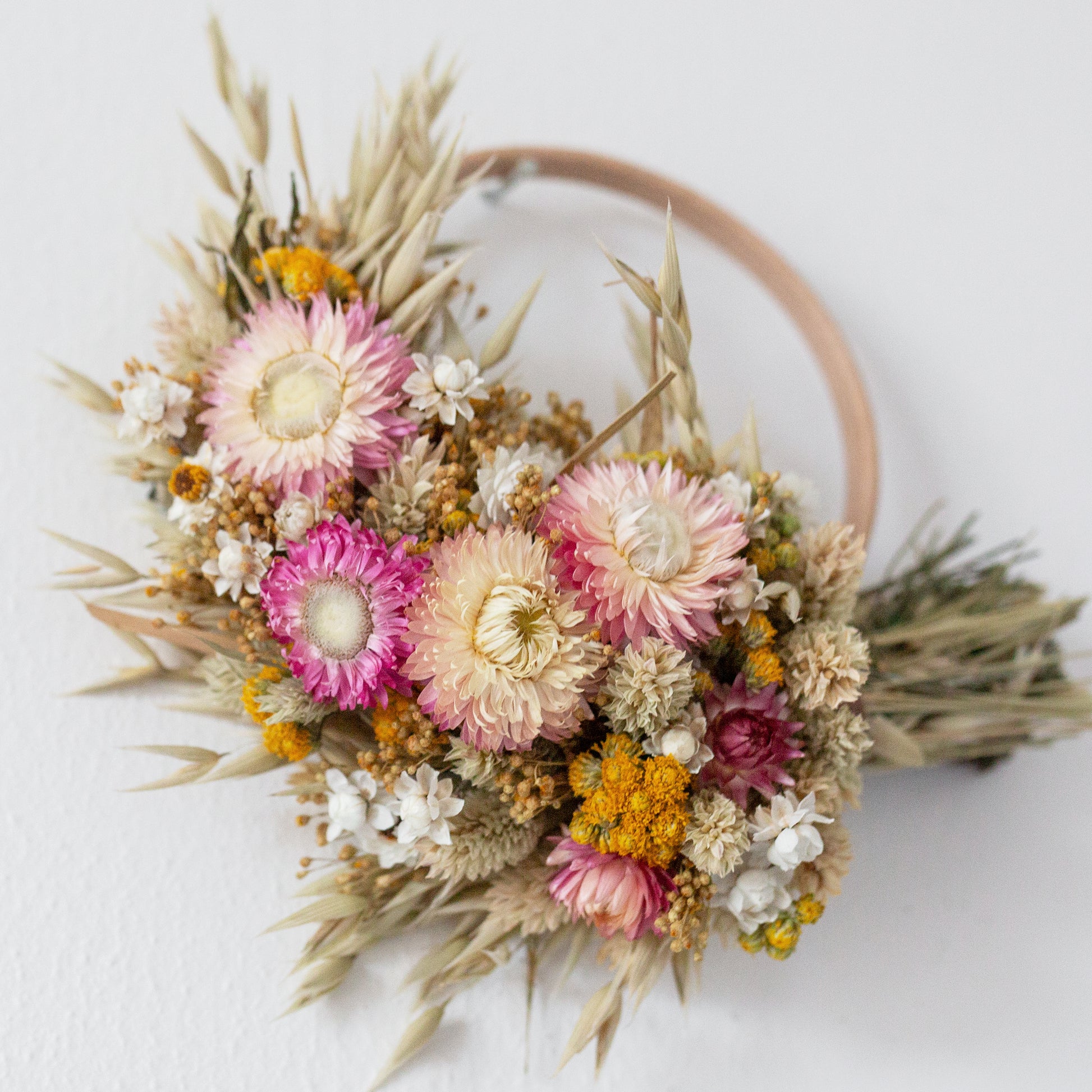 close up of pink and yellow dried flower wreath half covered in flowers. 
