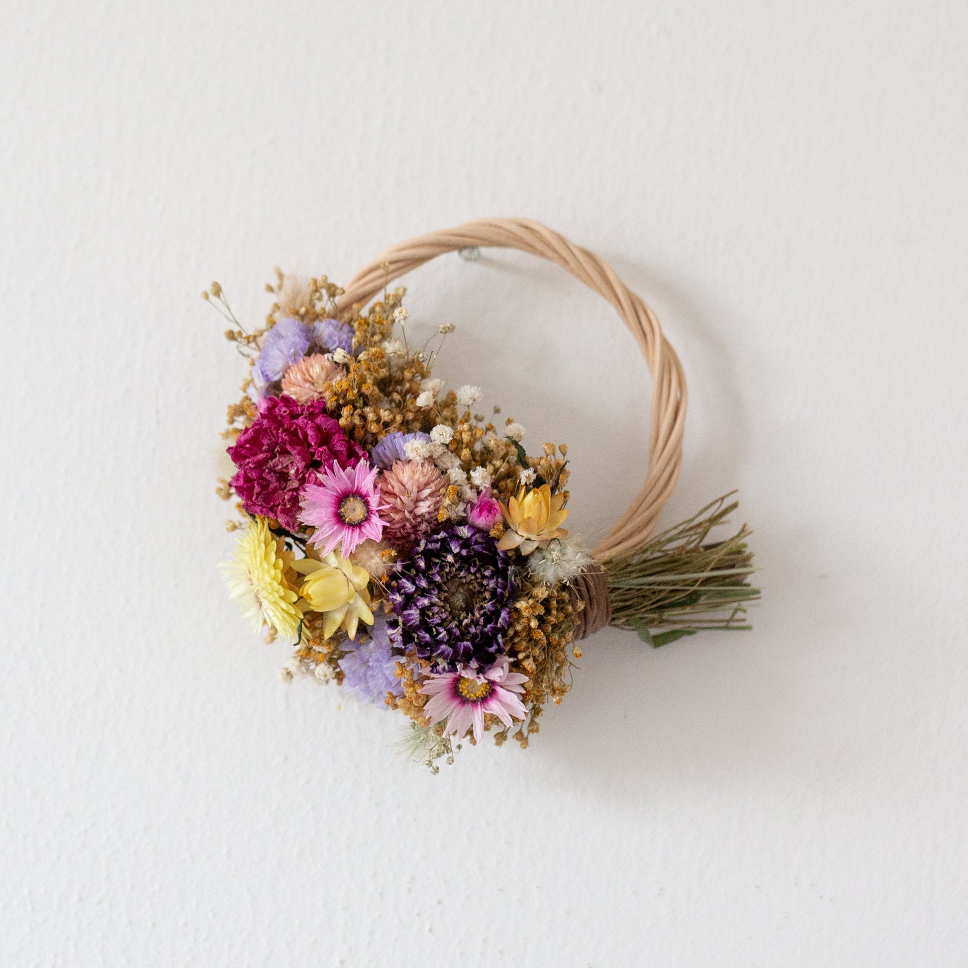 wicker wreath half covered in flowers hung on a white wall