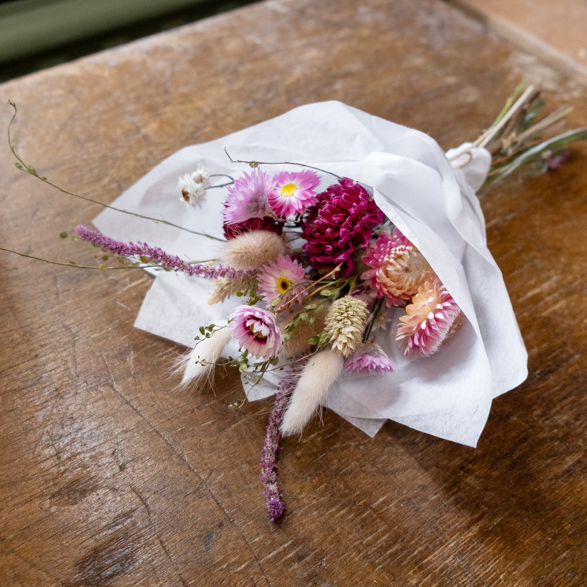 dahlia and strawflower dried flower posy laid on a table wrapped in tissue paper and tied with twine