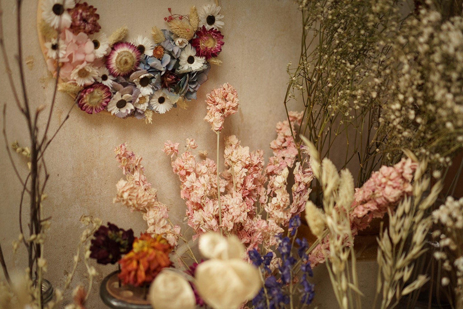 dried flower bunches in vases and jars in a florist studio setting, with a flower head embroidery hoop with linen background and flower heads pinks and blues stuck on