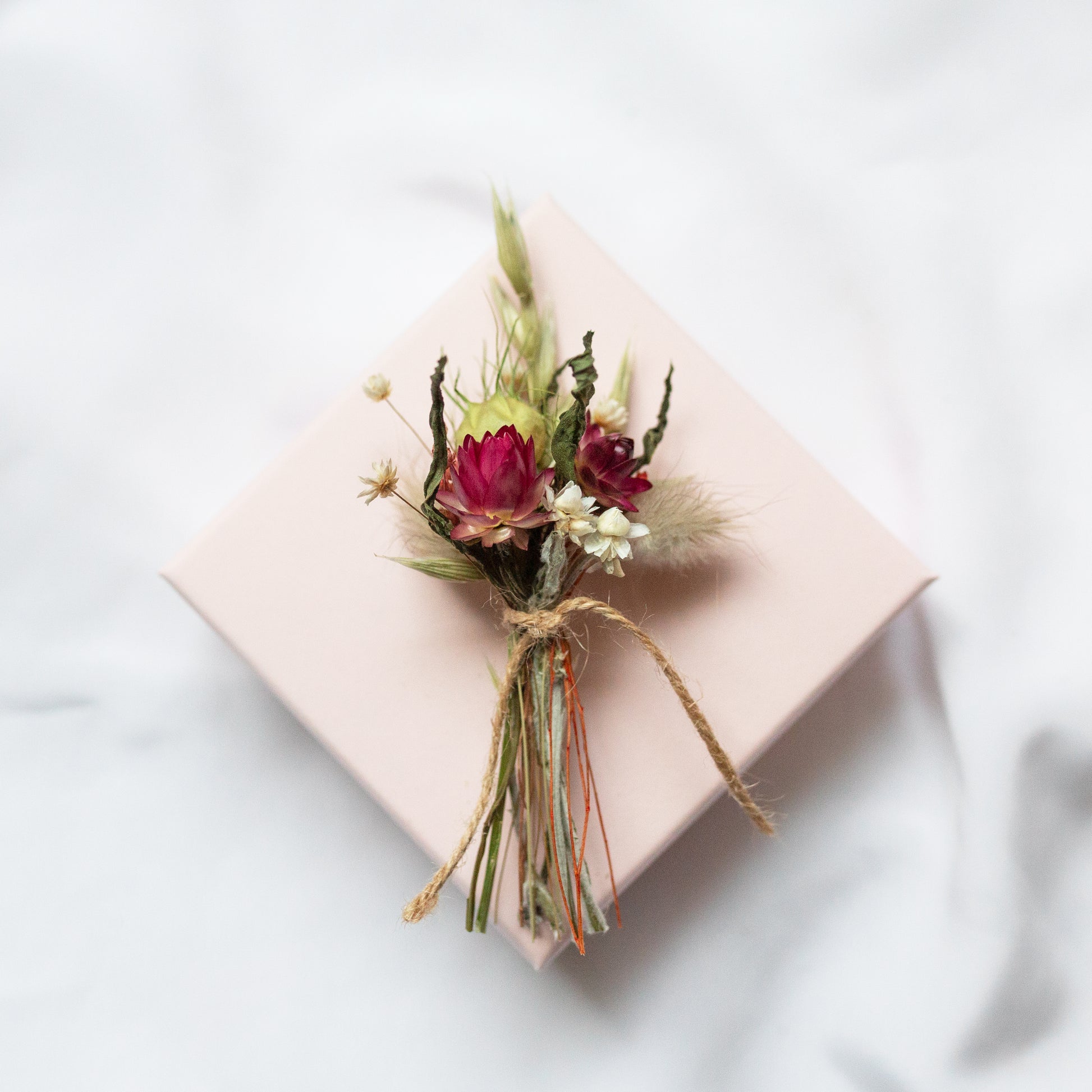 dried flower posy floral arrangement tied together with twine laid on a pink gift box on a white background