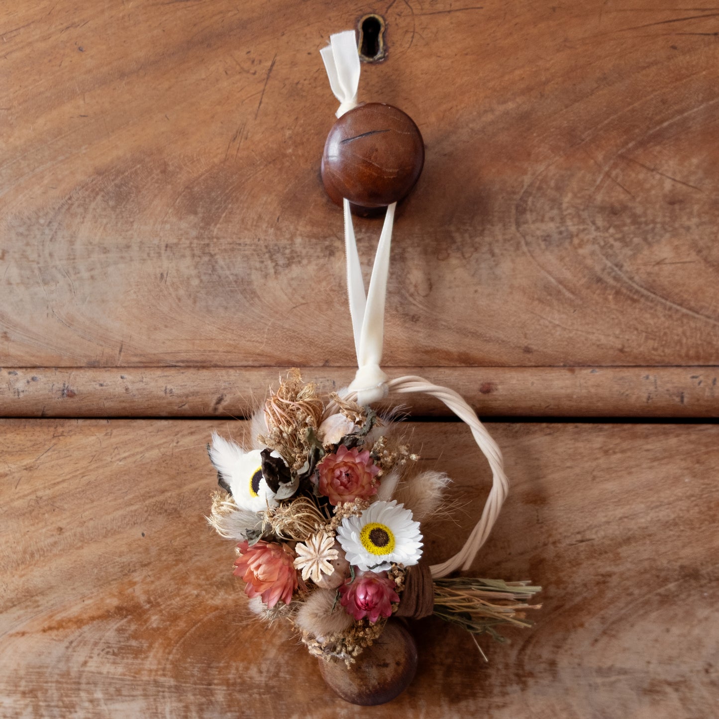 Decorative dried flower half wreath hanging hung on a wooden drawer by a cream velvet ribbon 