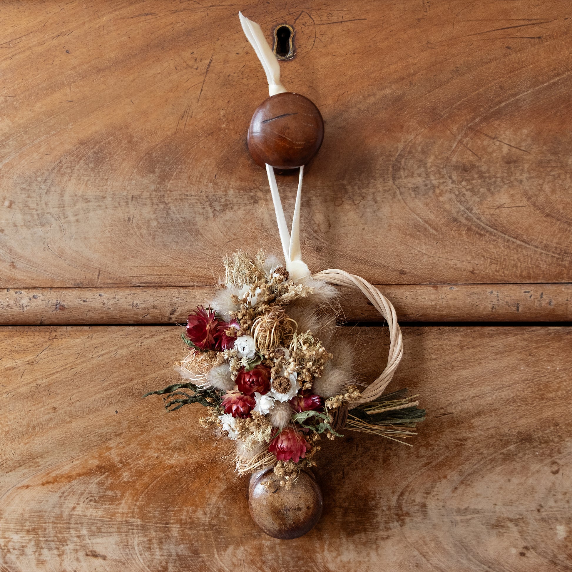 red and natural golden flower festive wreath decoration hanging from a cream ribbon on a drawer handle