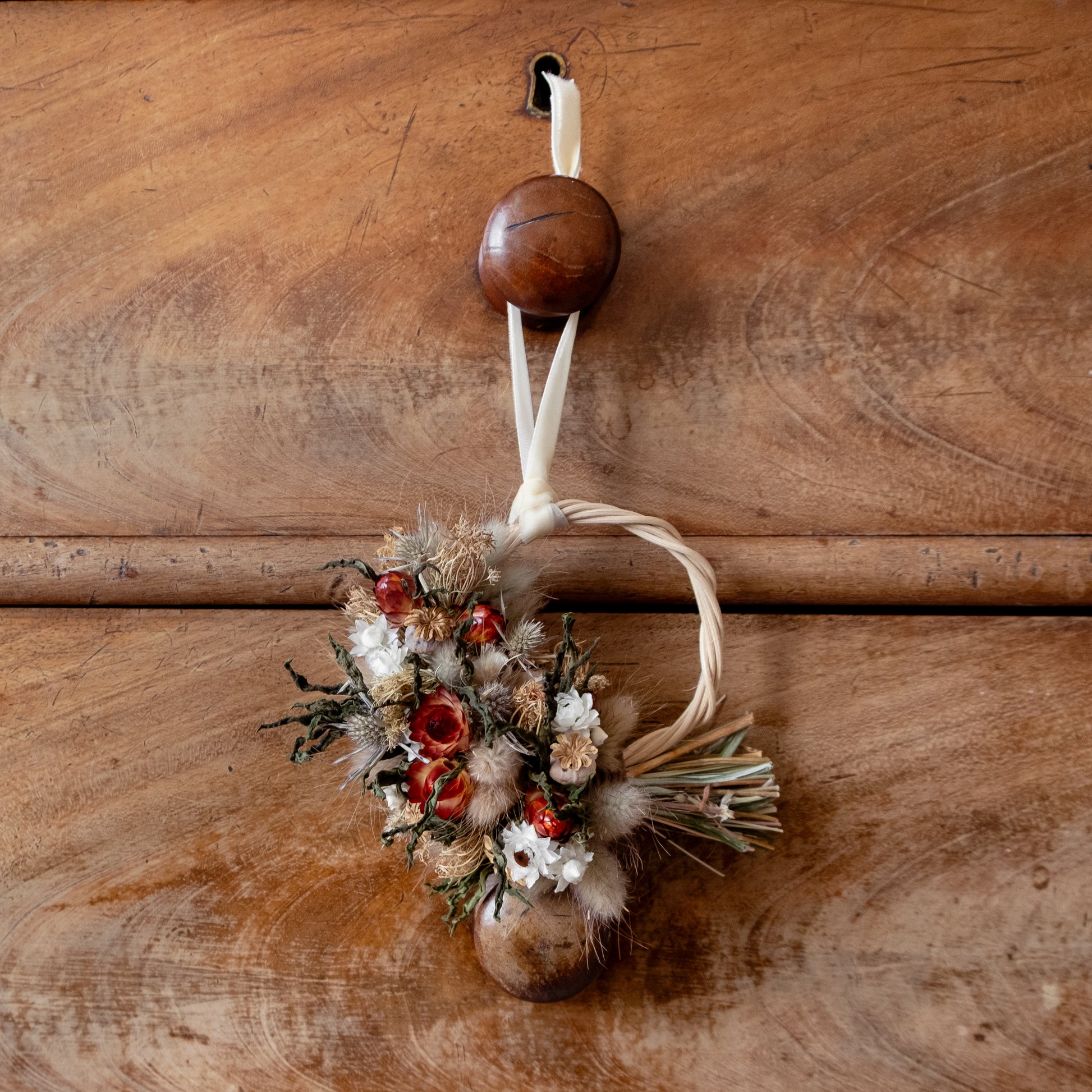 mini  festive half wicker wreath hung with a cream velvet ribbon on a wooden draw knob