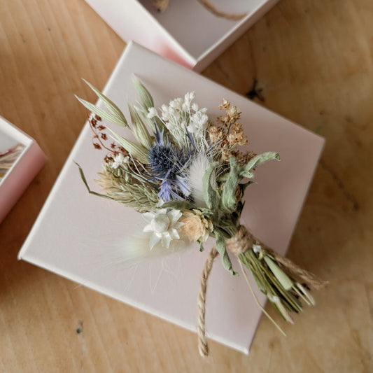 dried flower posy blue, white and neutral colour flowers. the posy is  laid on top of a pale pink gift box