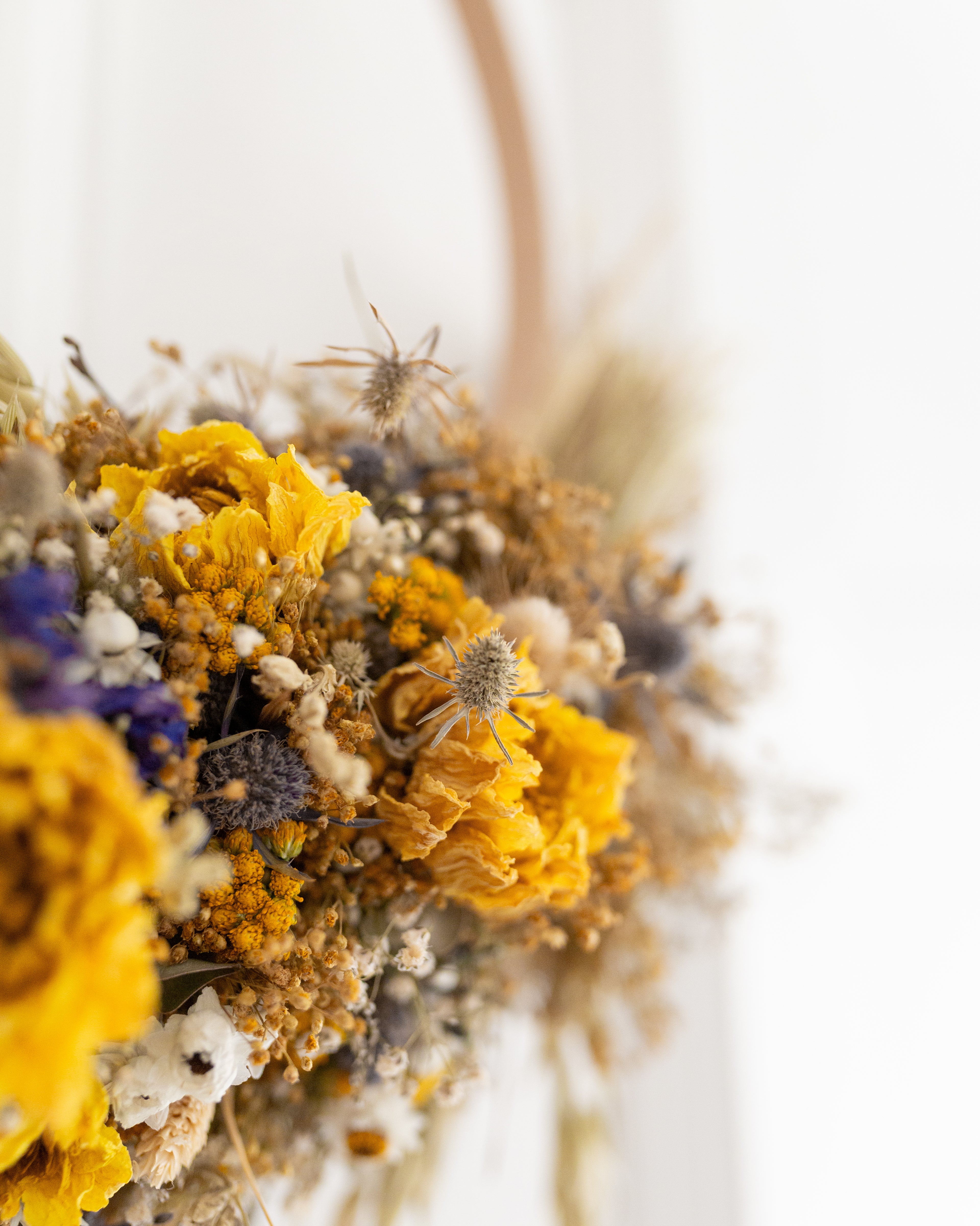 close up of dried blue thistles and yellow dahlias flowers in a yellow blue and white wreath. 
