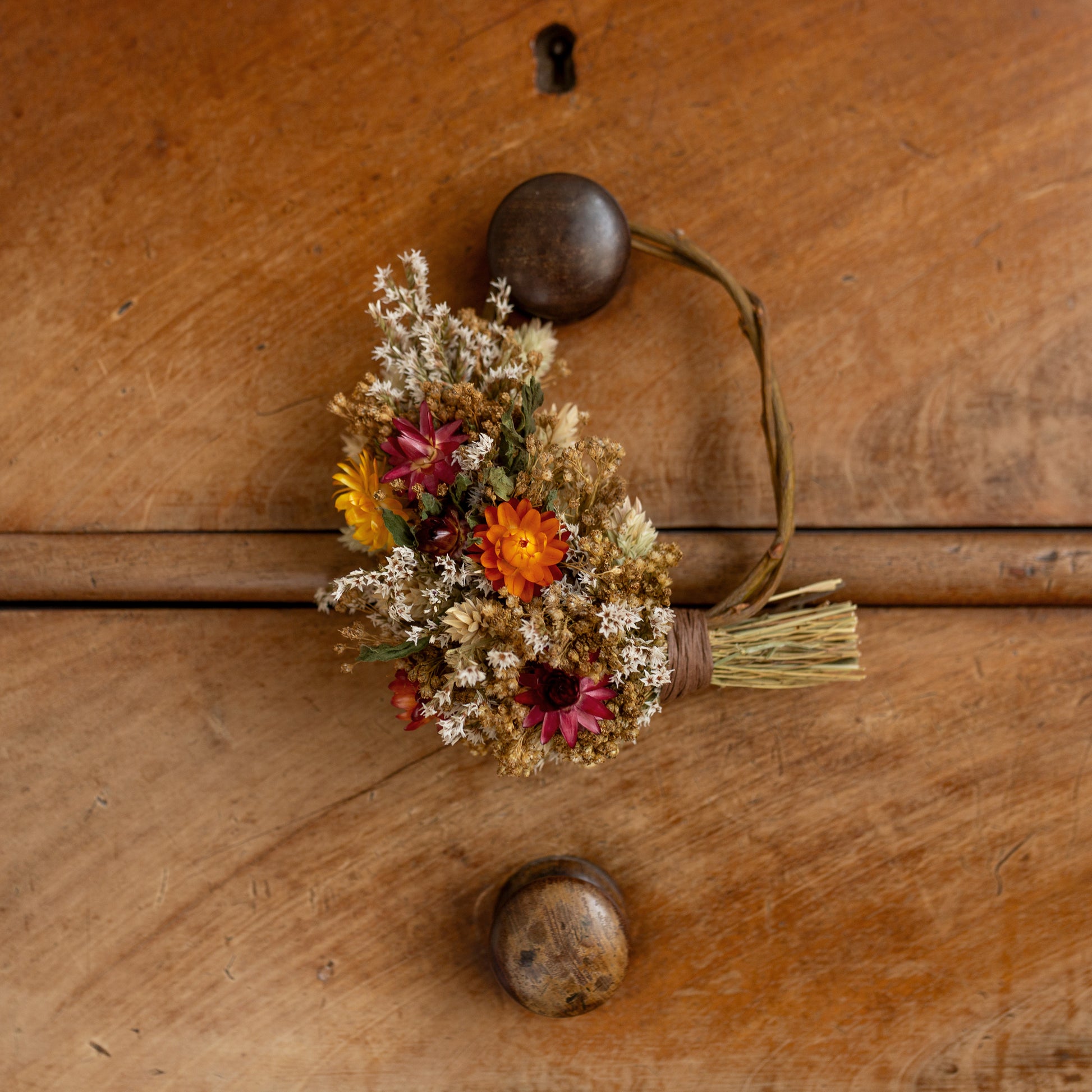 mini willow wreath, half covered in dried flowers. the wreath is hung on a wooden drawer knob
