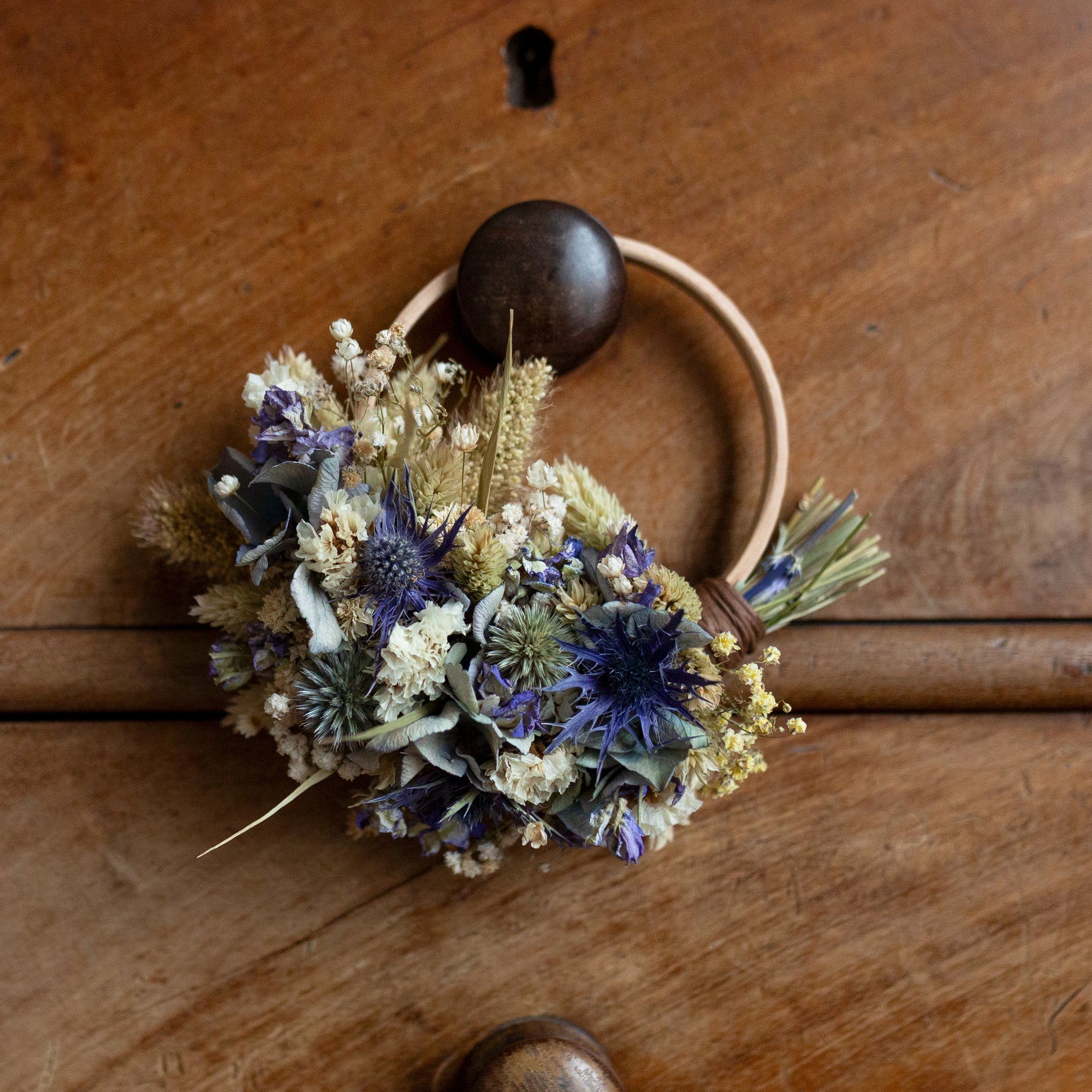 blue and white dried flower mini wreath hoop hung on wooden drawer knob. Flowers cover half of a wooden hoop 