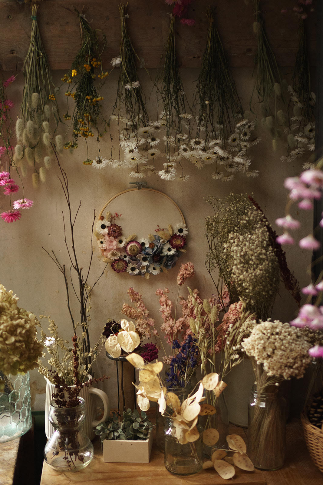 Decorative display of dried and fresh flowers in vases and hanging on a wall.