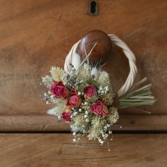 mini wicker wreath half covered in dried flowers, pink roses, lavender, Gypsophila. The wreath is hung on a drawer knob