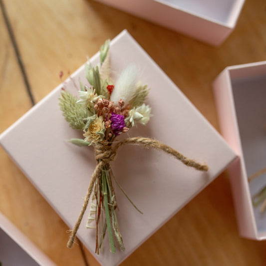 a dried flower pink and white gift size posy tied together with twine on top of a pale pink gift box