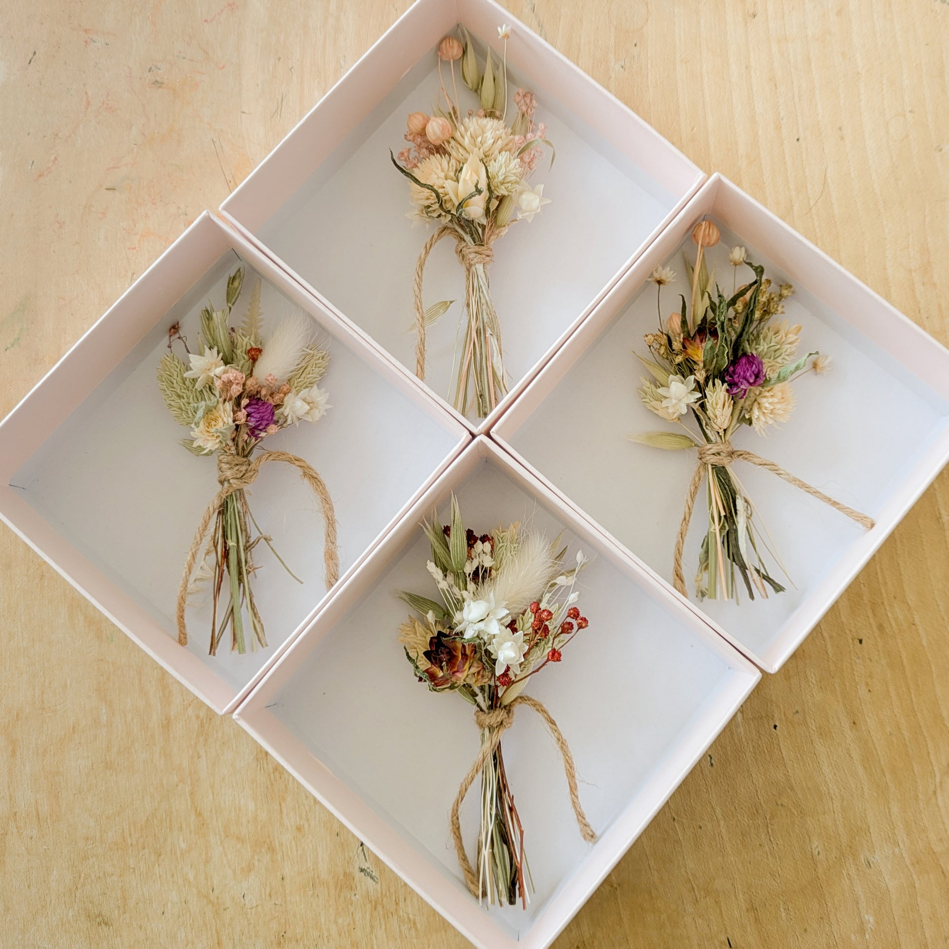 4 pink gift boxes set out in a diamond shape, each contain a dried flower mini posy tied together with twine