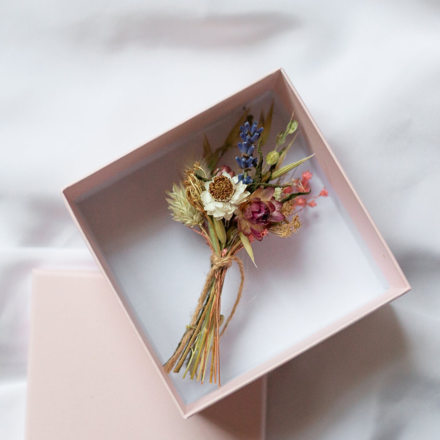 mini posy blue, red, white and green flowers and grasses laid in a gift box with white insides and pale pink outsidr