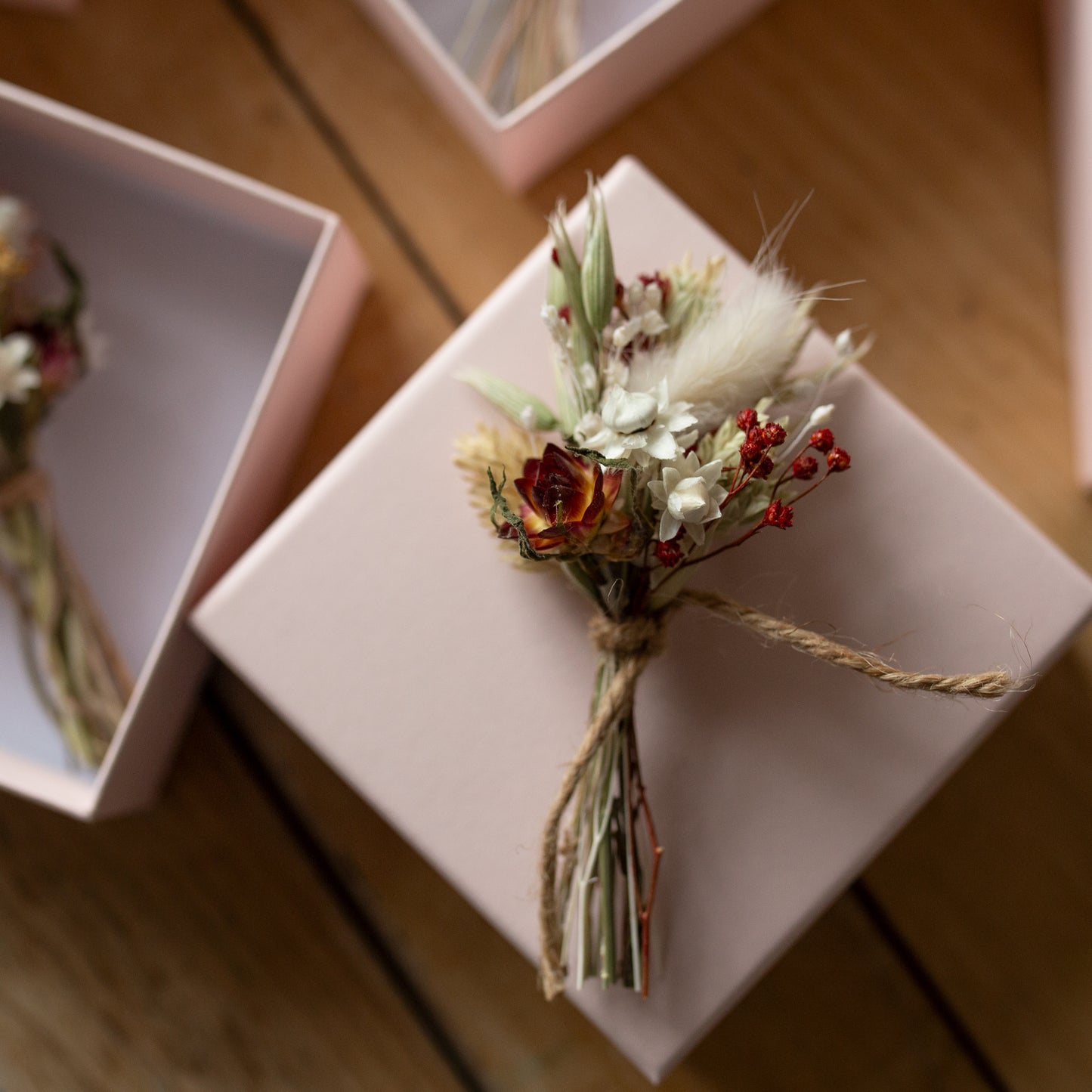 red and white dried flower posy tied together with twine on top of a pink gift box