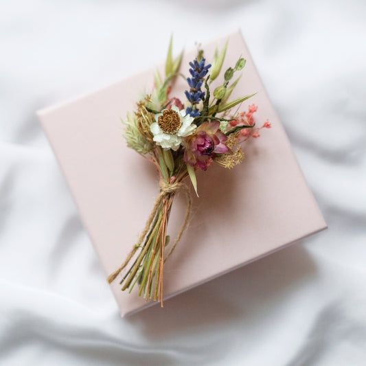 mini pink strawflower, white winged daisy and lavender posy tied with twine laid on a pink gift box