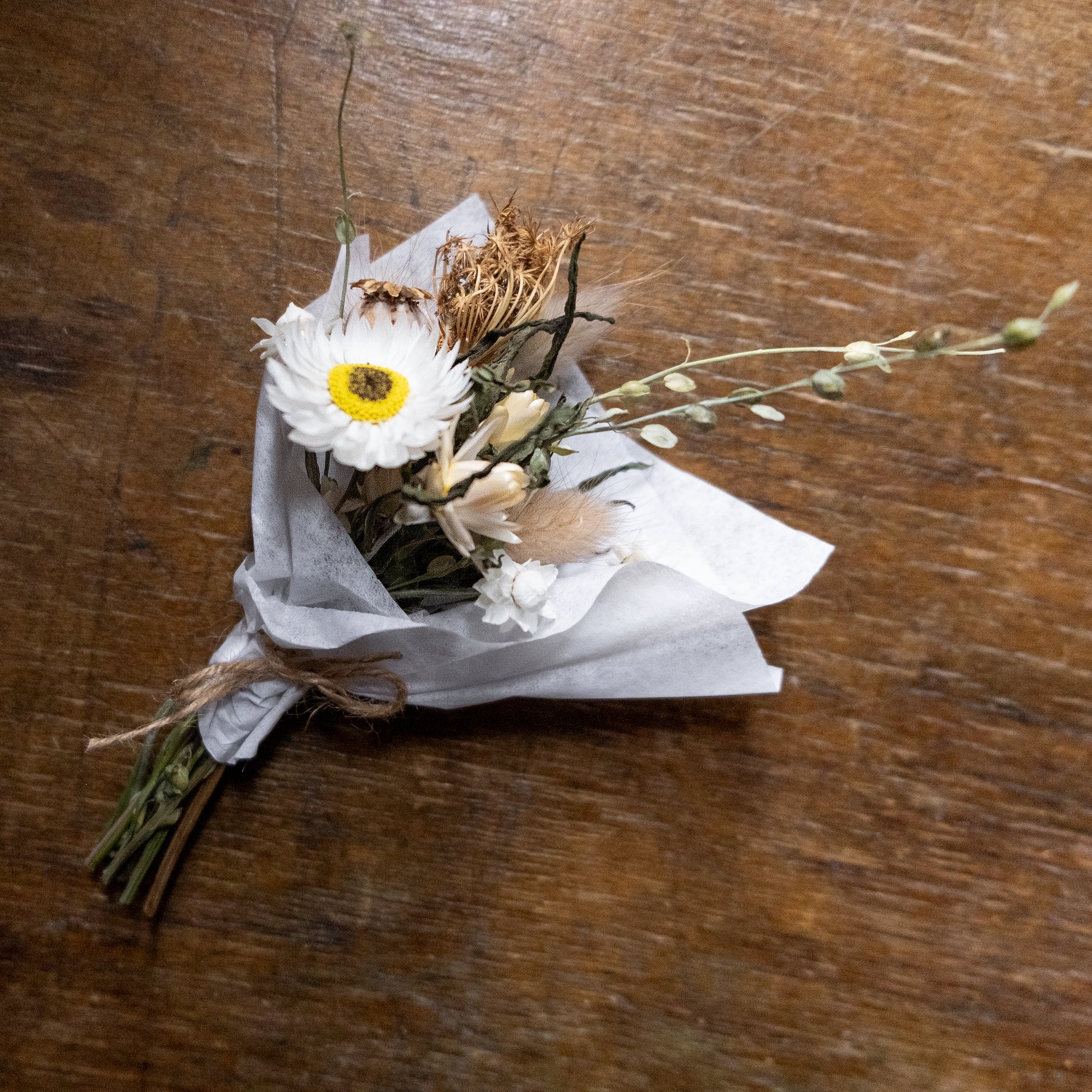  a white, green flower posy in on a wooden surface wrapped in white tissue paper tied with twine