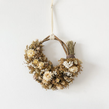 neutral white and golden dried flower wreath hung on a white wall