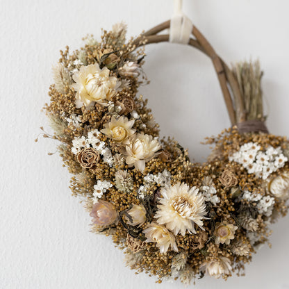  close up of a neutral dried flower wreath of white strawflowers and ixodia daisies, natural golden broom bloom filler and creamy roses. 