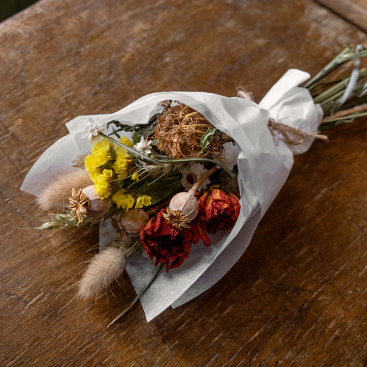 dried flower posy small bouquet on a wooden surface. the posy is tie together and wrapped in tissue