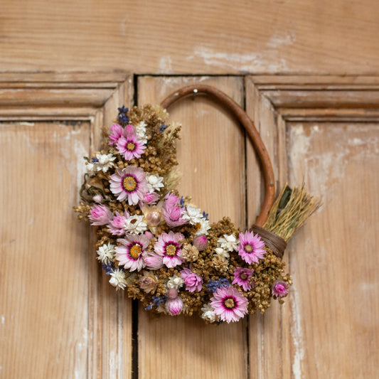pink and white daisy wreath with lavender and golden filler. the wreath is half covered in flowers with a willow hoop. it is hung on the back of an old wooden door