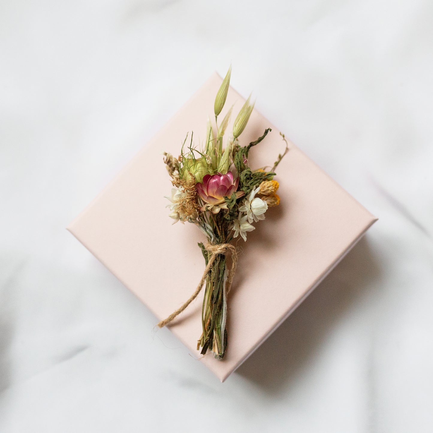 mini posy made of dried flowers tied with twine laid on a pink box on a white background