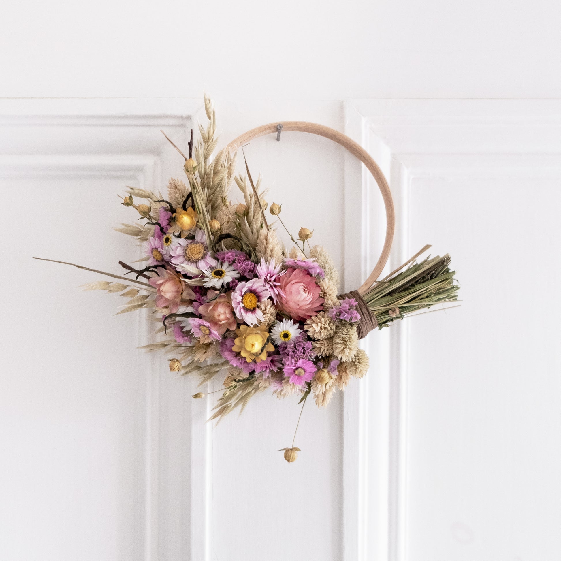small pink and yellow wreath half covered in flowers hung on the back of a white door