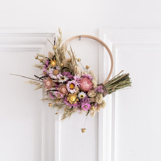 small pink and yellow wreath half covered in flowers hung on the back of a white door