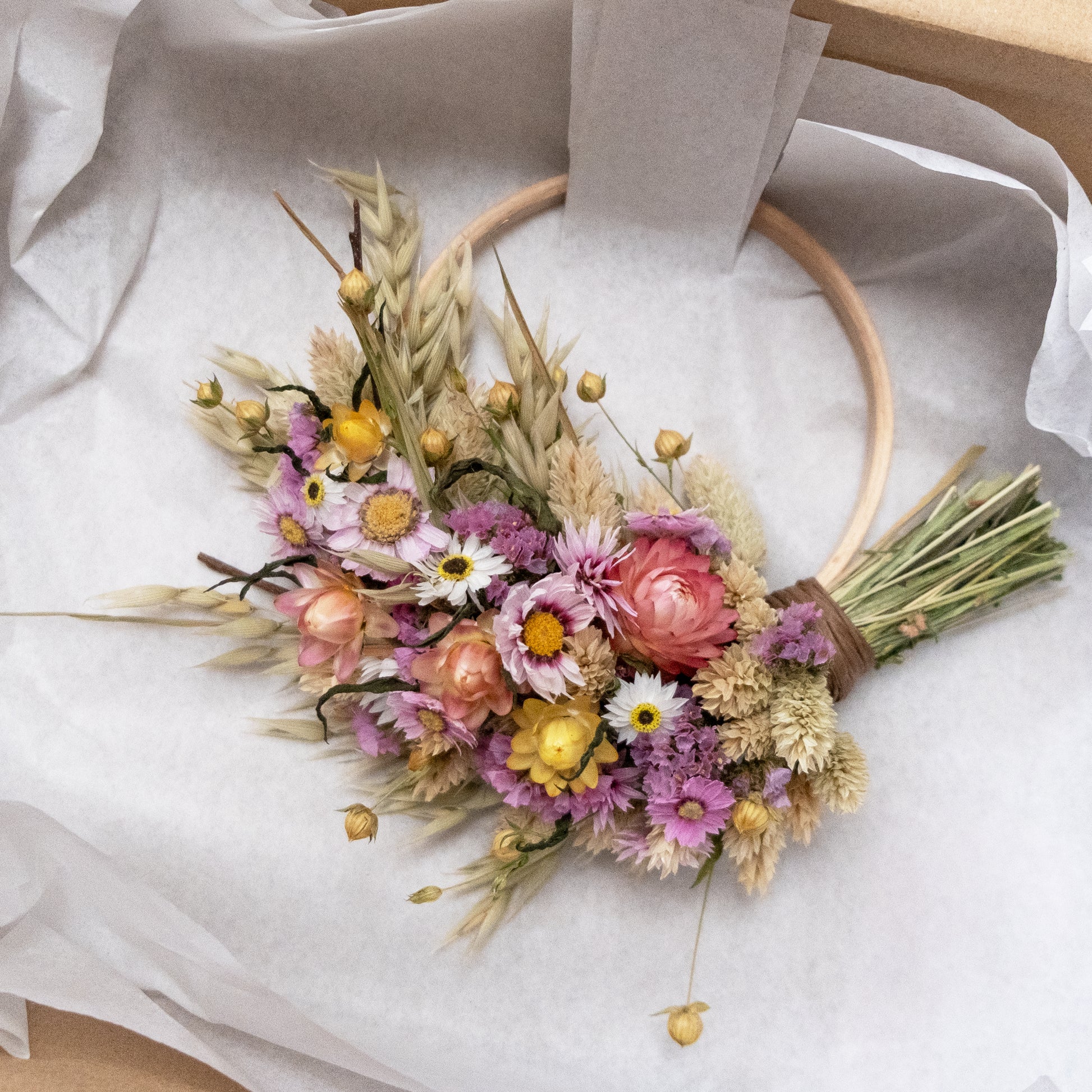 pink and yellow strawflower wreath secured in a kraft box with white tissue 