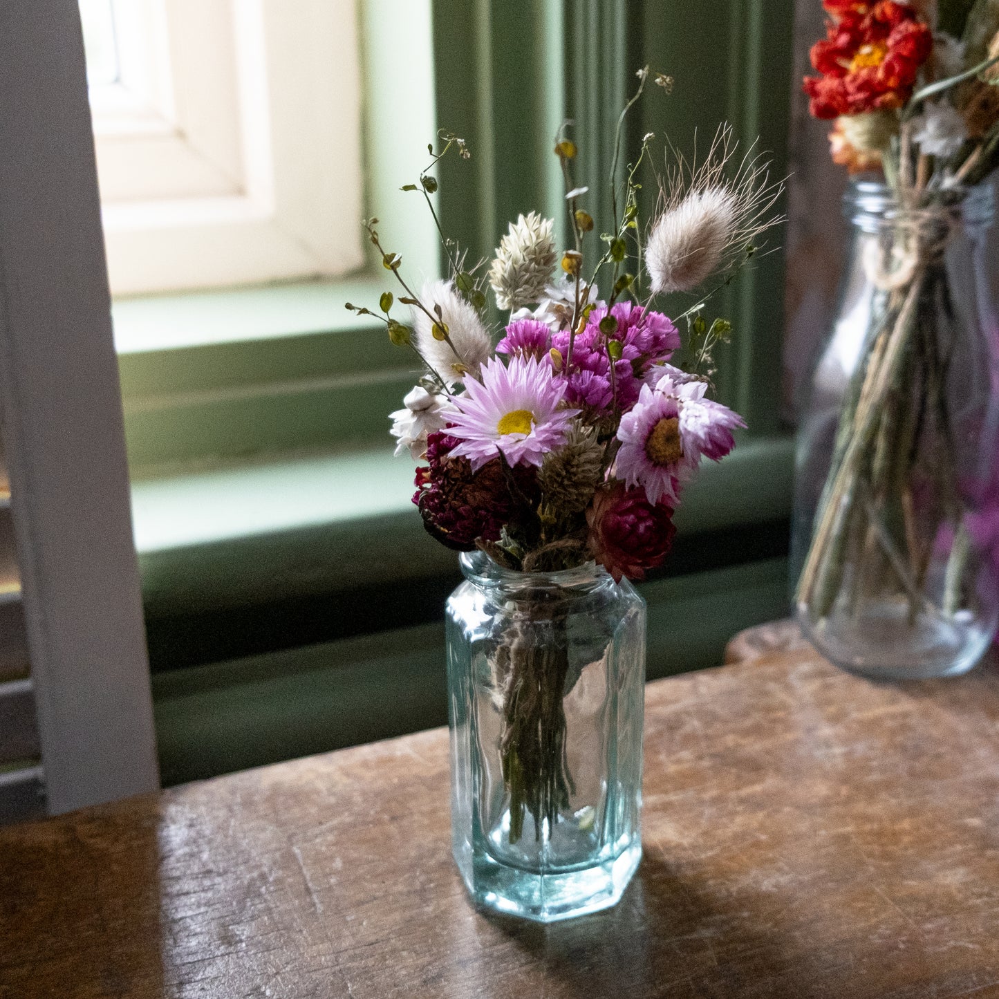 glass clear bud vase on a wooden table with a pink flower posy inside