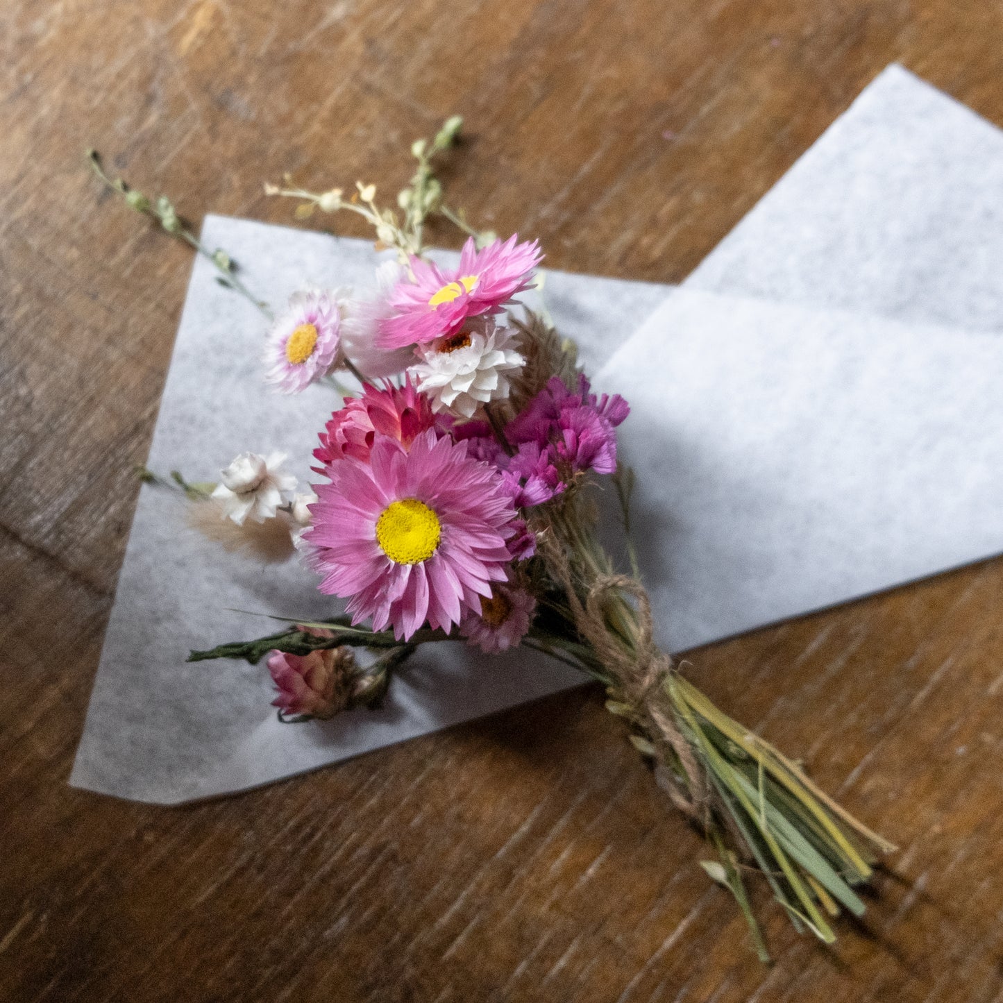 Small bouquet of pink and white flowers laid on white tissue ready to be wrapped on a wooden table