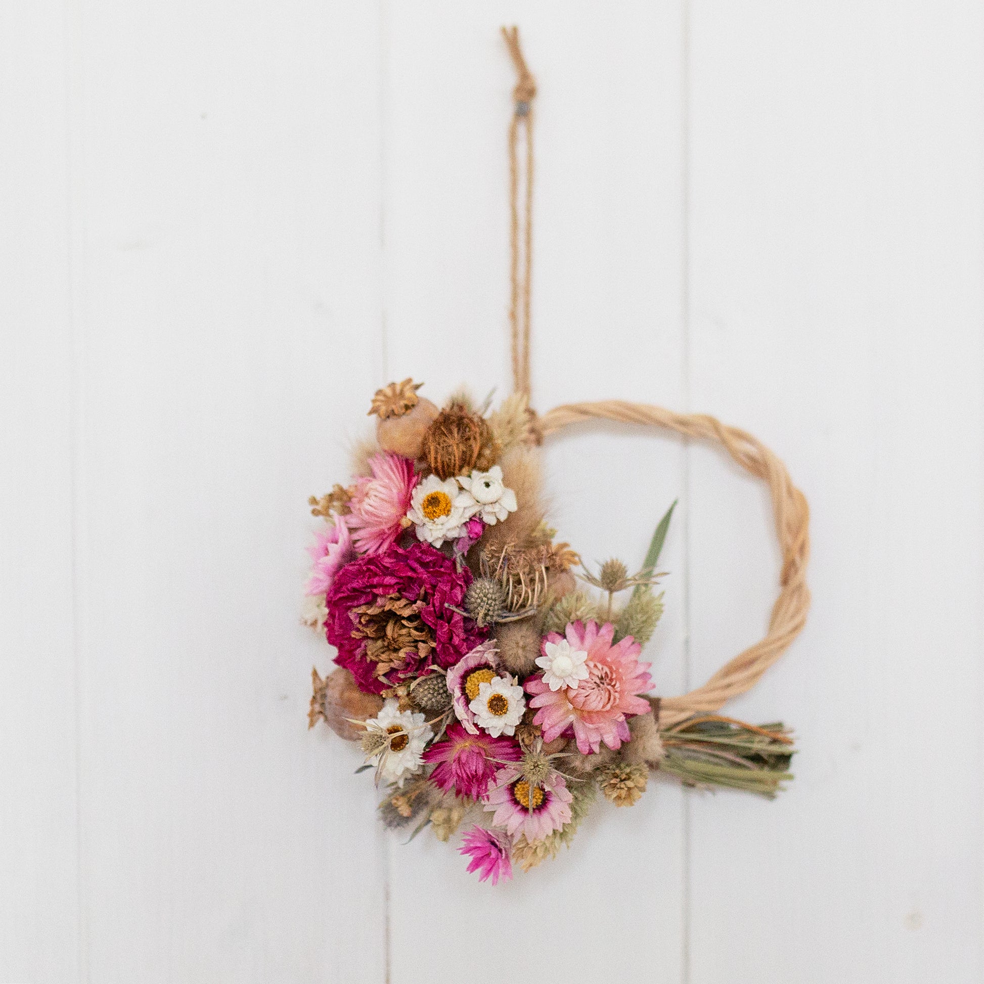 Decorative dried flower wreath made with pink and white flowers, hung via twine on a white wooden panelled background