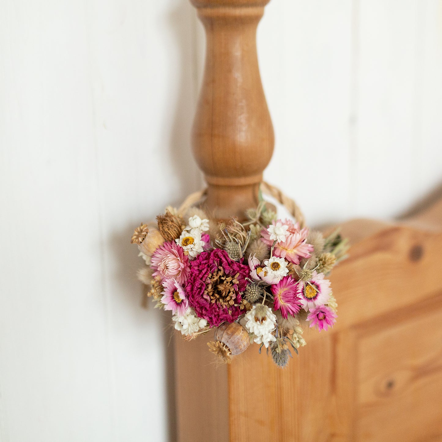pink and white dried flower wreath arrangement hung on a vintage pine bed post against a white wooden panelled wall
