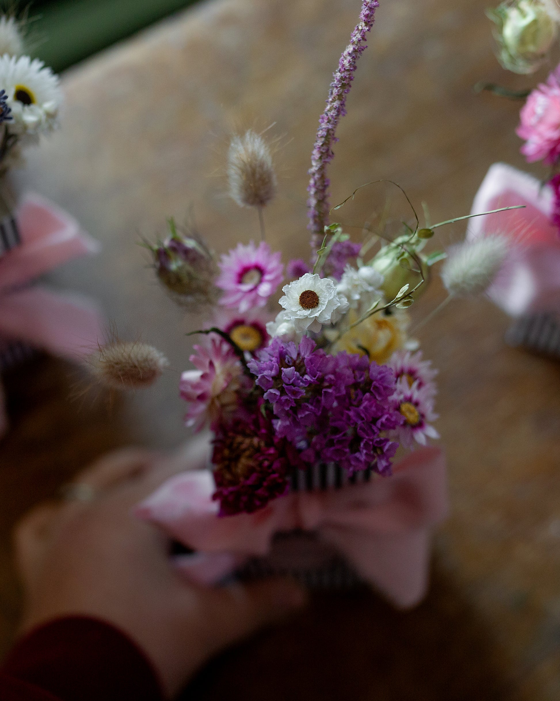 Small bouquet of flowers with pink flowers held in a hand placed on a wooden surface